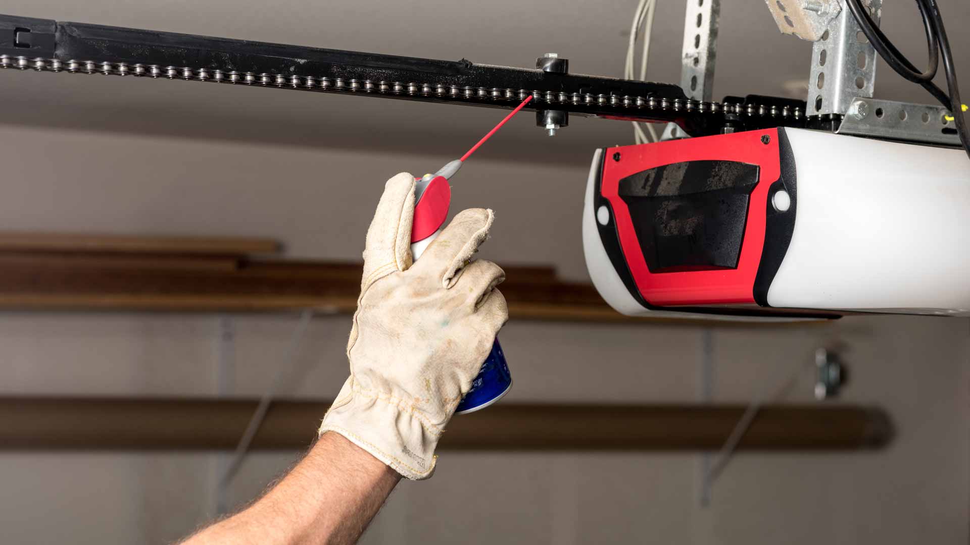 Close-up shot of man applying WD-40 to chain on garage door opener